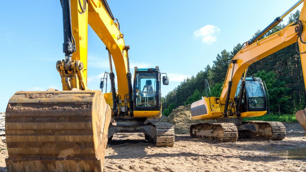 Máquinas pesadas sendo usadas em obras, na imagem duas escavadeiras.